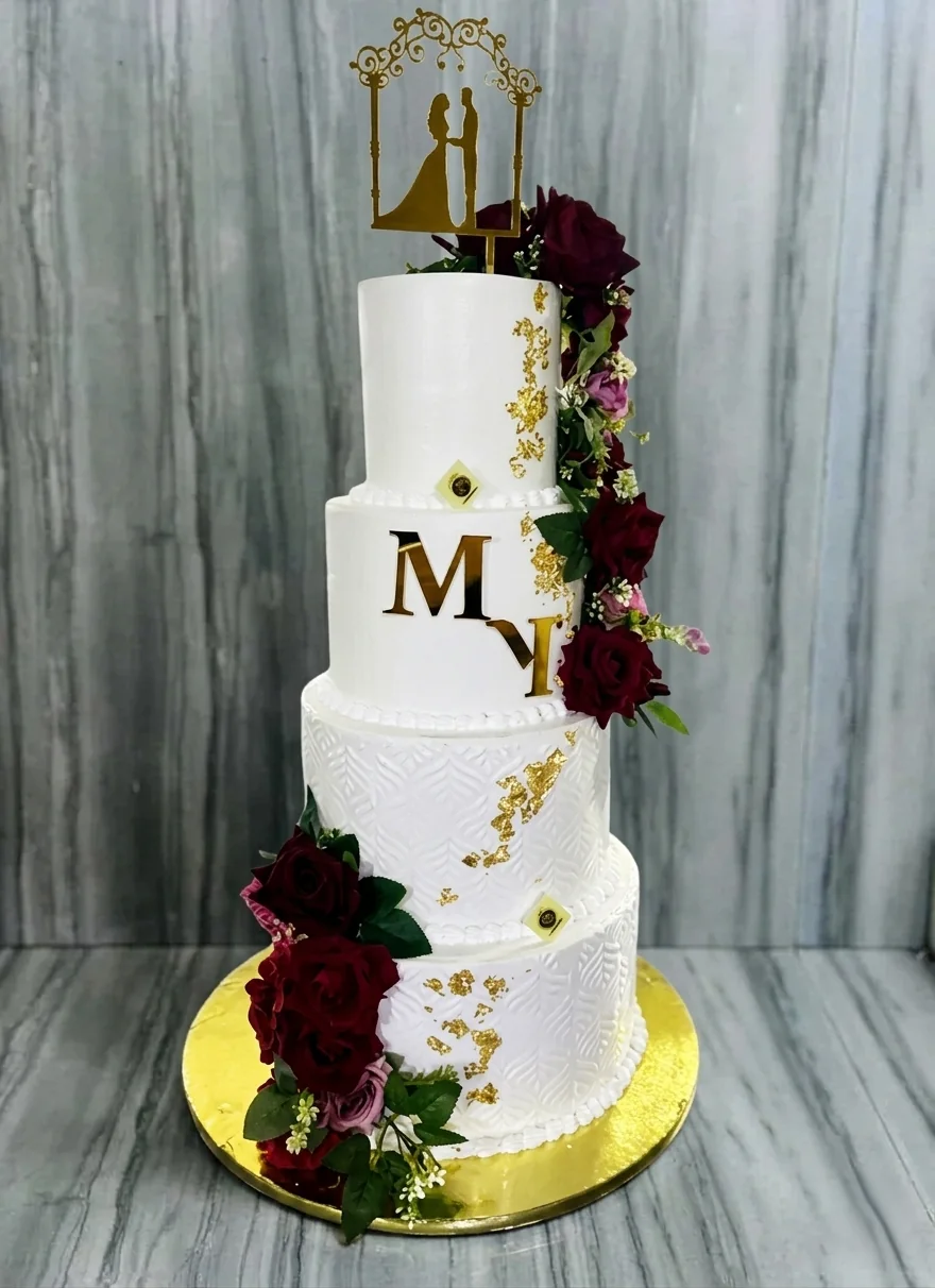 Pièce montée de mariage à quatre étages, roses rouges fraîches, éclats de feuille d'or et monogramme doré.