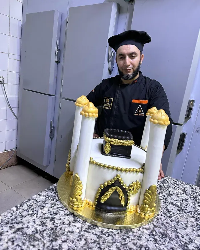 Gâteau blanc inspiré de la Kaaba, quatre colonnes et ornements dorés sculptés, présenté par le chef.