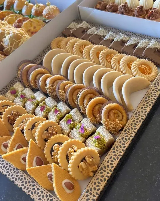 Plateau de pâtisseries marocaines de mariage, cornes de gazelle, briouates et gâteaux aux amandes rangés en lignes.